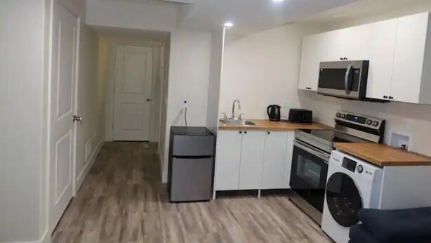 A compact kitchen with a refrigerator, microwave, oven, and washing machine.