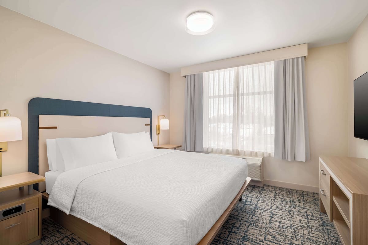 A hotel room with a large bed, bedside tables, a flat-screen TV, a window with curtains, and a ceiling light.