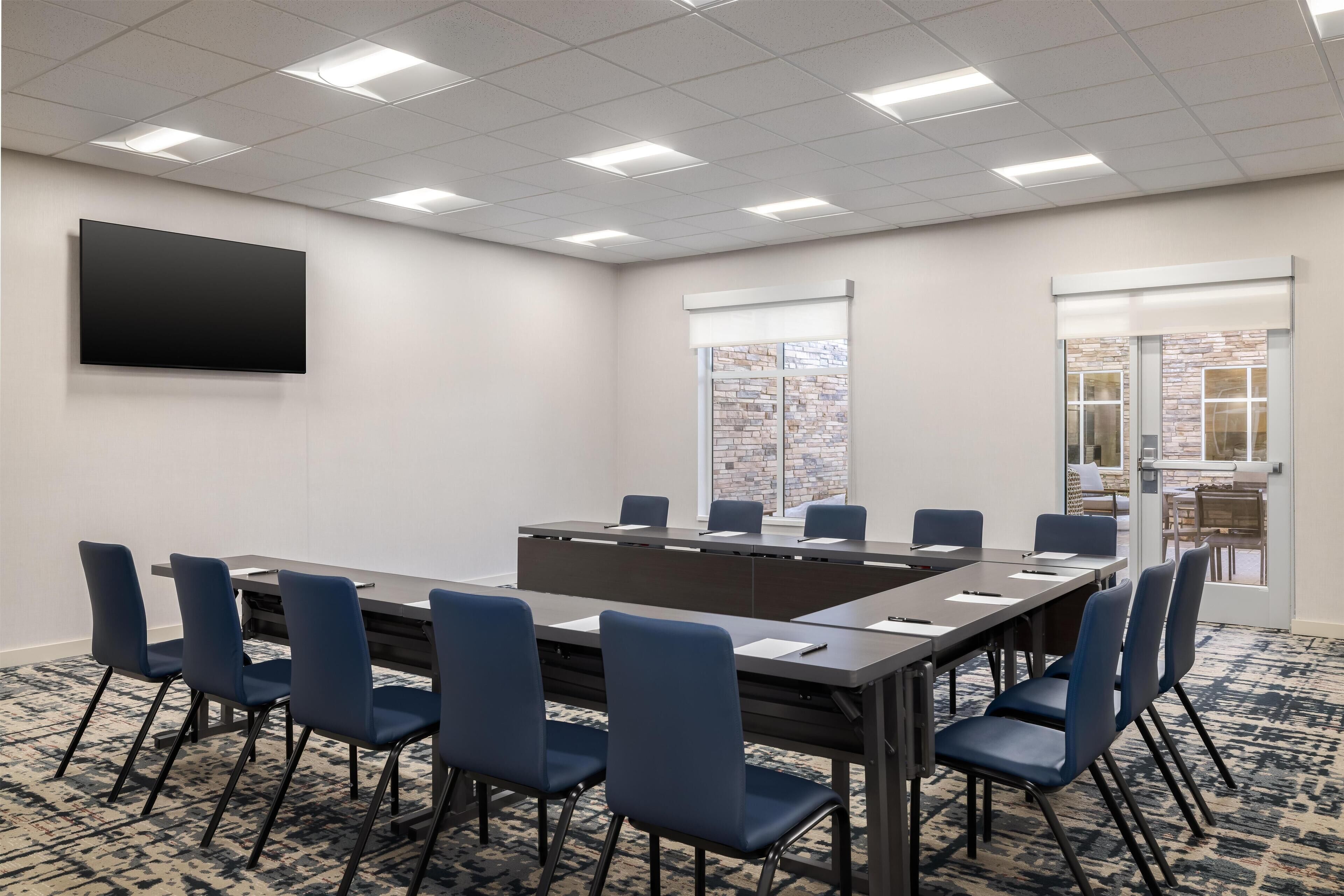 A conference room with a long table, blue chairs, a flat-screen TV, and a patterned carpet.