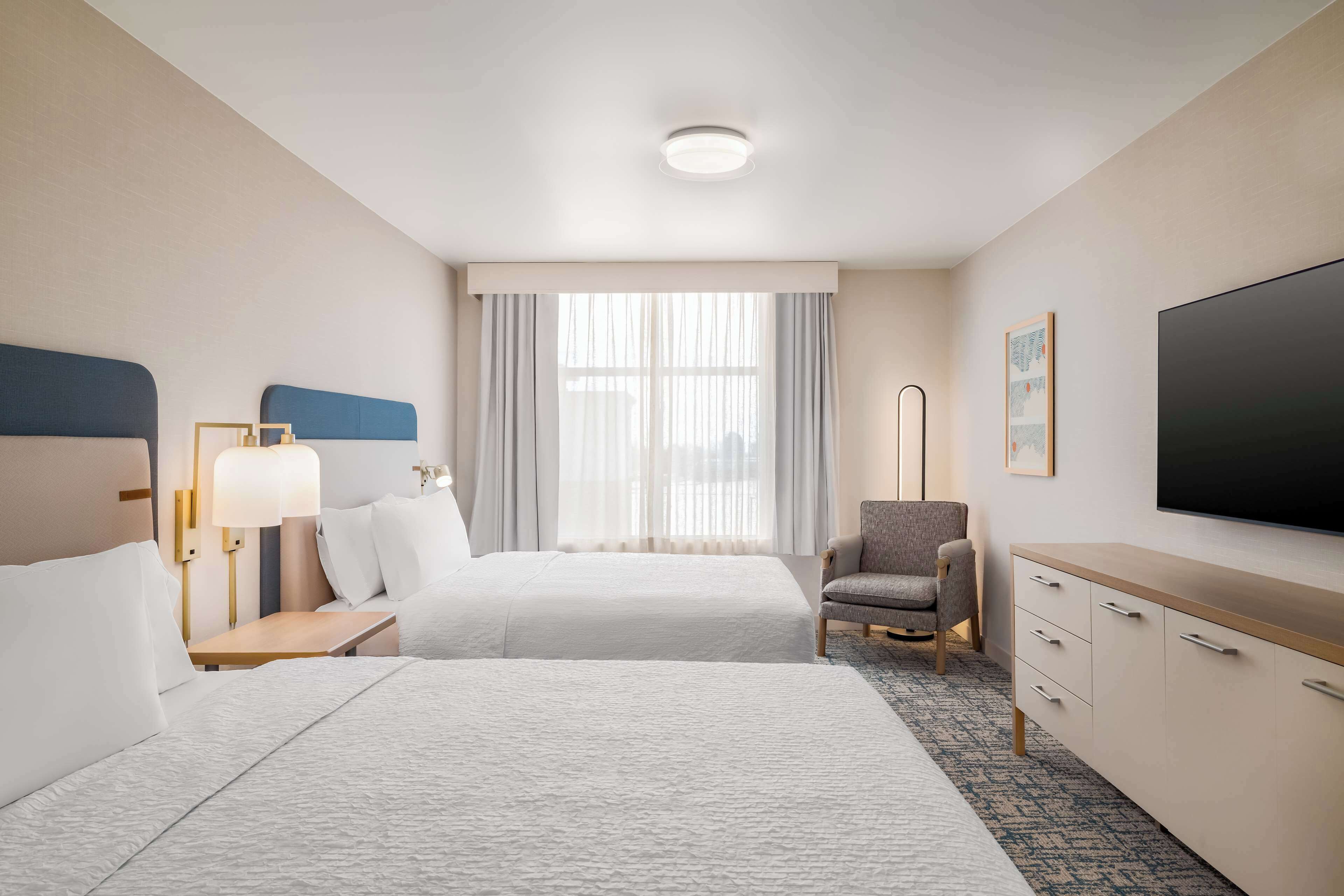 A hotel room with two beds, a desk, a chair, a TV, and a window with curtains.