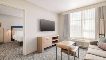 Quarto de hotel com cama, televisão, escrivaninha, cadeira, sofá e uma grande janela.