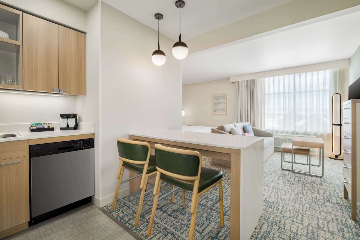 A modern kitchen with a dishwasher, two bar stools, a central island, and a dining area with a table and chairs.