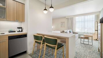 A modern kitchen with a dishwasher, two bar stools, a central island, and a dining area with a table and chairs.