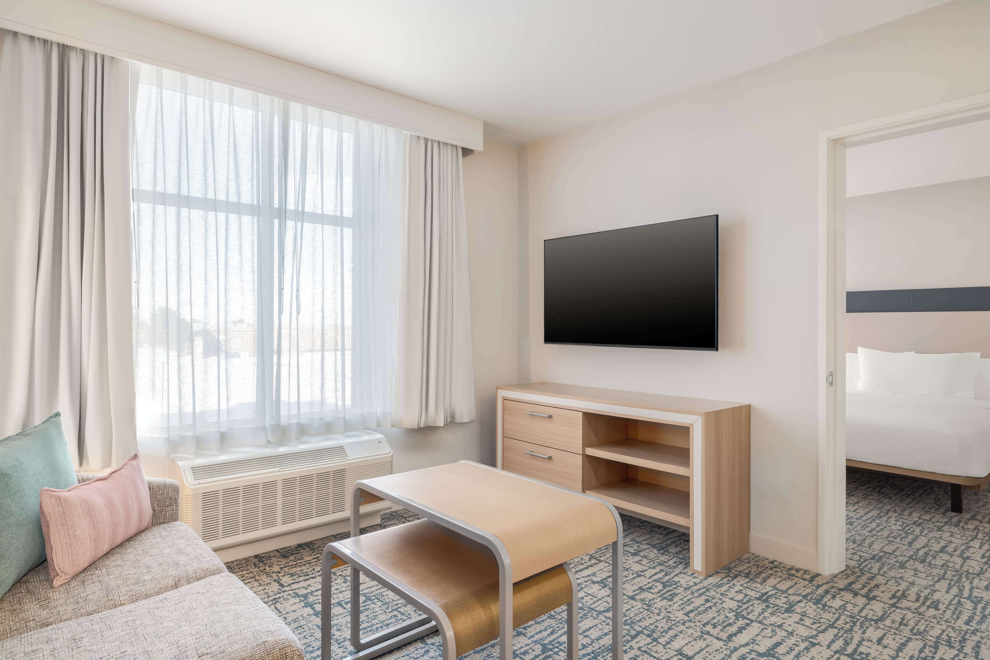 A hotel room with a bed, a TV, a desk, and a window with curtains.