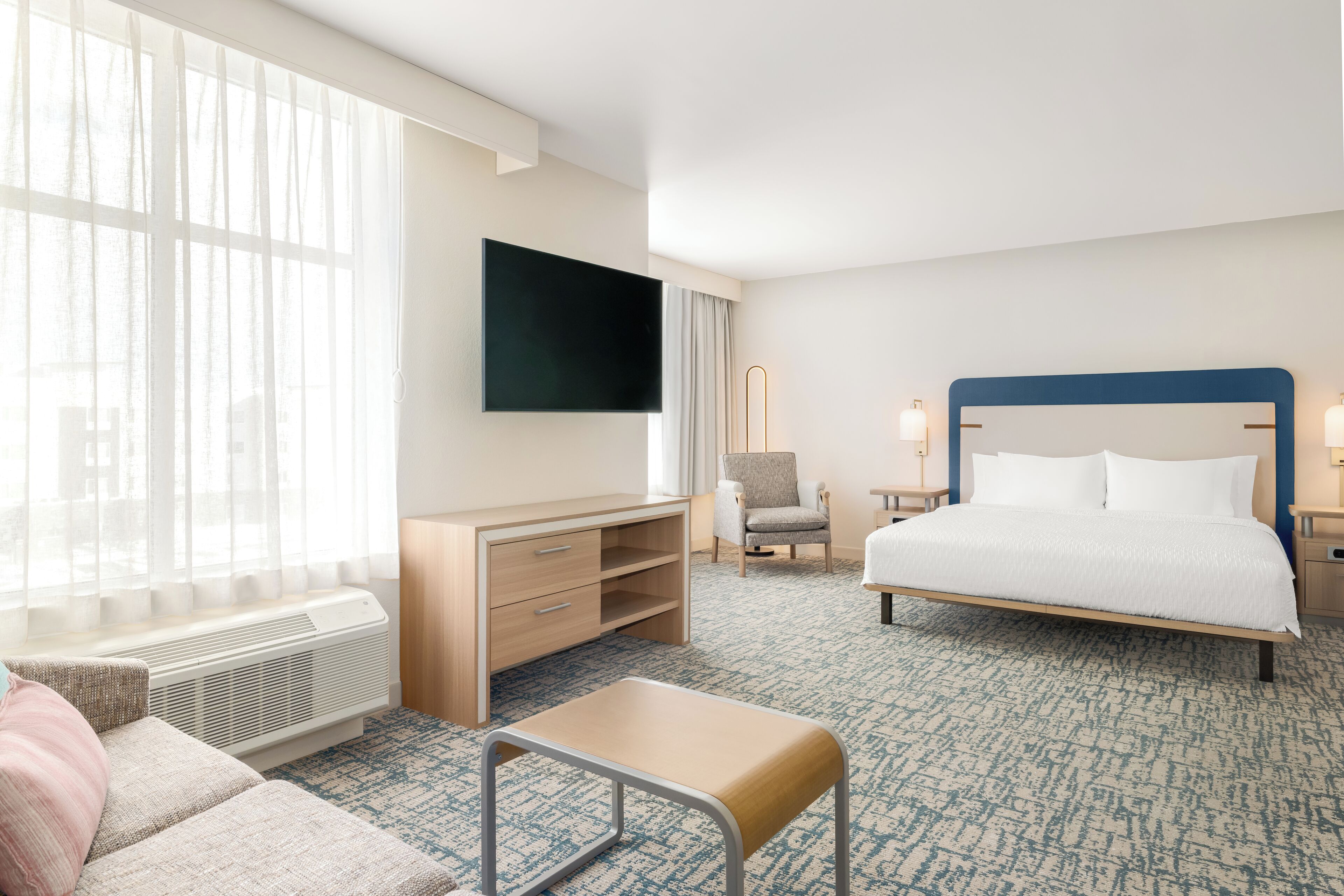 A hotel room with a bed, a desk, a chair, a TV, and a window with curtains.