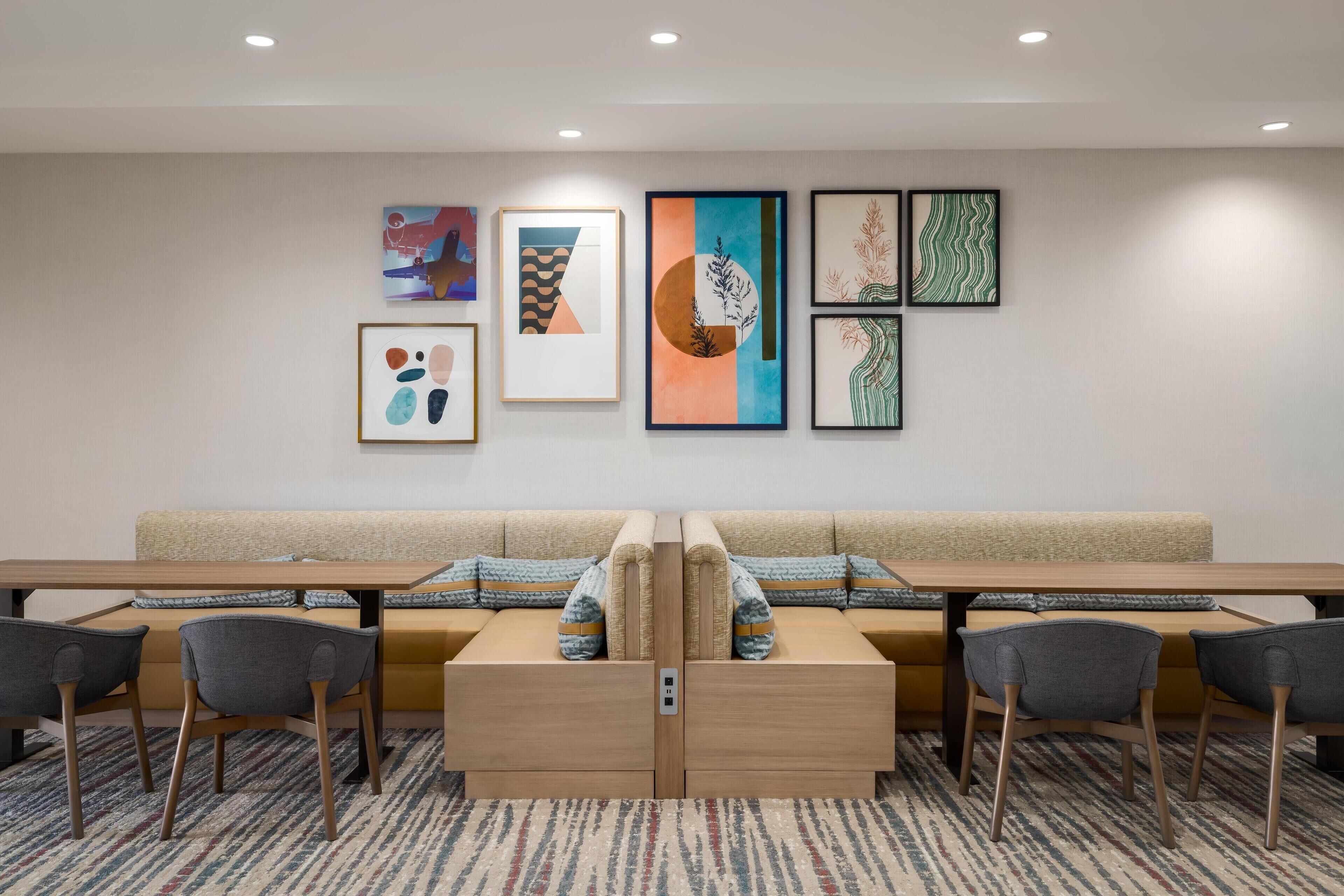 A modern hotel room with a long wooden table, two sofas, and a patterned carpet.