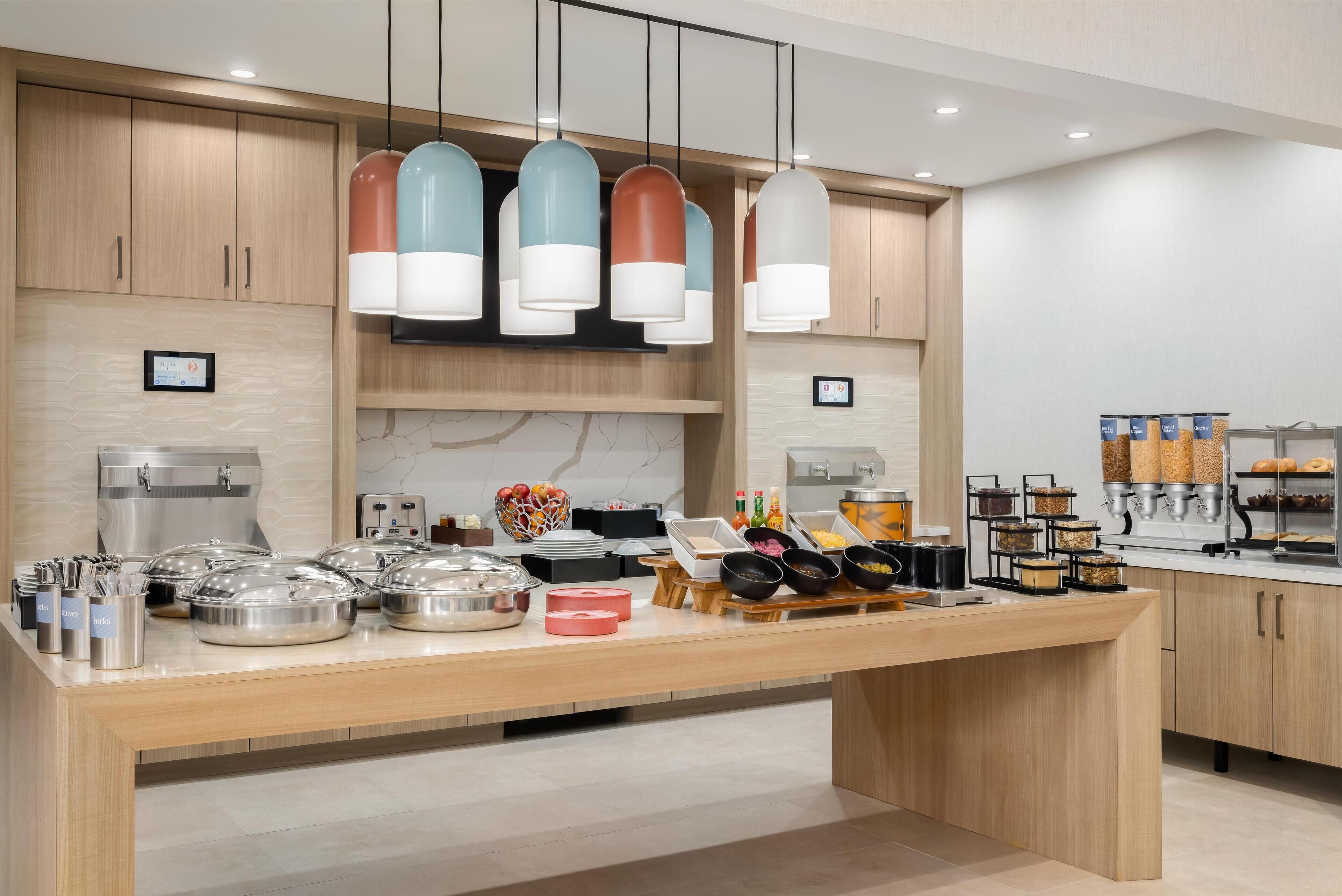 A modern kitchen with wooden cabinets, a breakfast bar, and various food items.