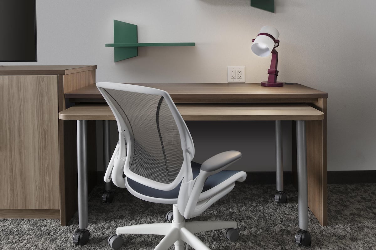 Un bureau moderne, doté d’une chaise de bureau à dossier en maille, d’un lampadaire et d’une étagère verte.