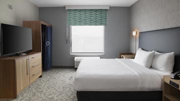A hotel room with a bed, a TV, a wardrobe, a bedside table, a lamp, and a window with a view.