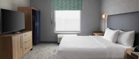 A hotel room with a bed, a TV, a wardrobe, a bedside table, a lamp, and a window with a view.