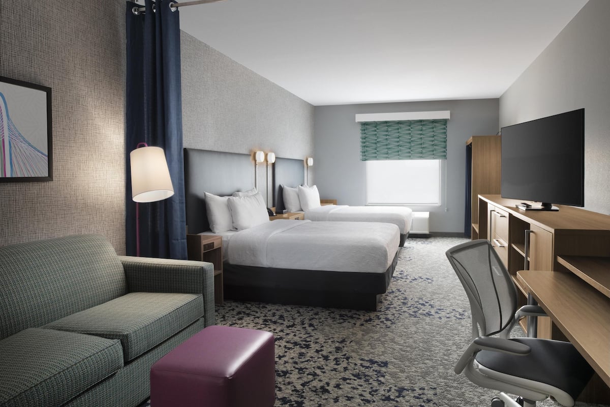 Une chambre d’hôtel avec deux lits, un bureau, une chaise, un canapé, une télévision et une lampe.
