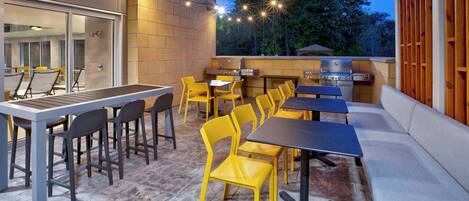 Eine Terrasse im Freien mit Grillplatz, gelben Stühlen und Tischen.