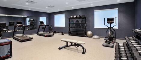 Een fitnessruimte met loopbanden, elliptische trainers, een bankje, gewichten en trainingsballen.