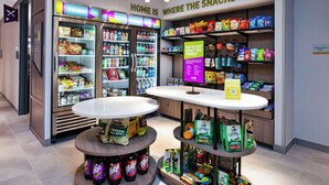 Un quiosco de aperitivos con gran variedad de bocadillos y bebidas, que incluye un refrigerador y una mesa con bolsas de papas y otros productos.