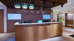 Un moderno área de recepción de hotel con un mostrador de madera, dos pantallas grandes y un letrero digital.