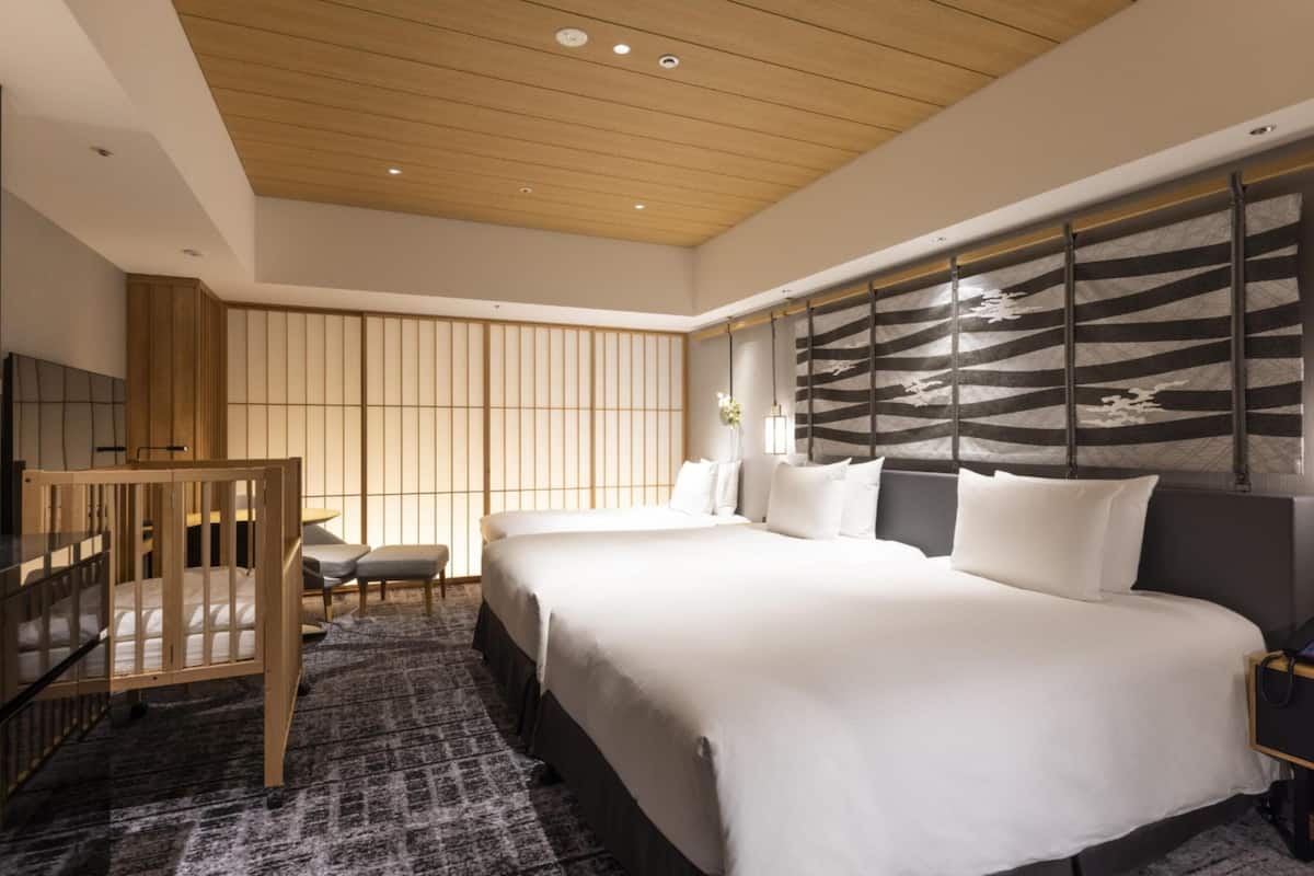 A modern hotel room with a large bed, a wooden crib, a seating area, and a decorative wall panel.