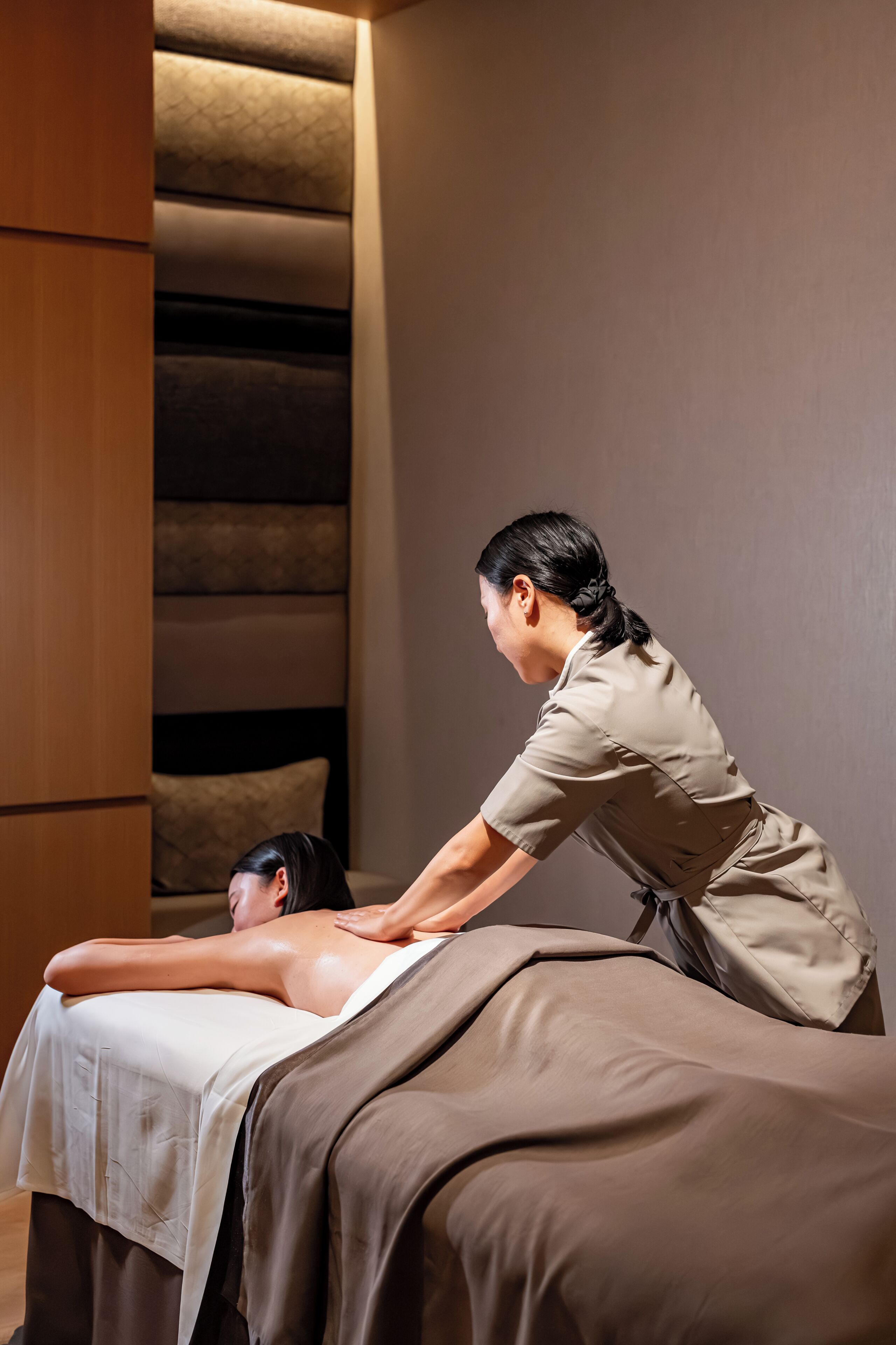 A massage therapy session in a room with a patterned wall and a wooden cabinet.