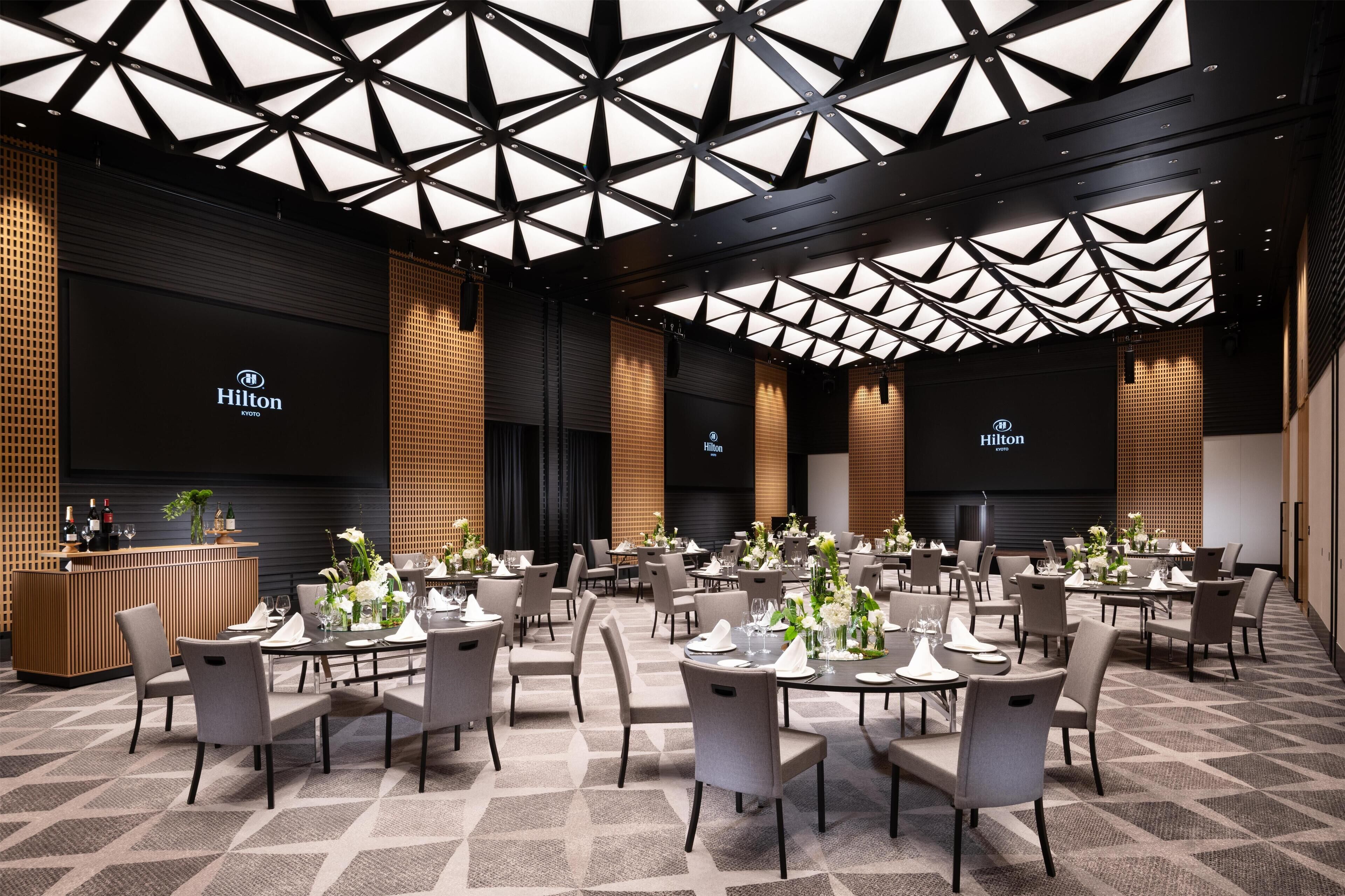 A spacious hotel dining area with multiple tables set for guests, a reception desk, and a modern ceiling design.
