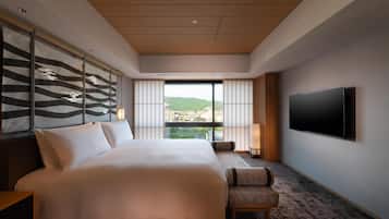 Ein Hotelzimmer mit einem großen Bett, einem an der Wand montierten Fernseher und Blick auf die Stadt durch große Fenster.