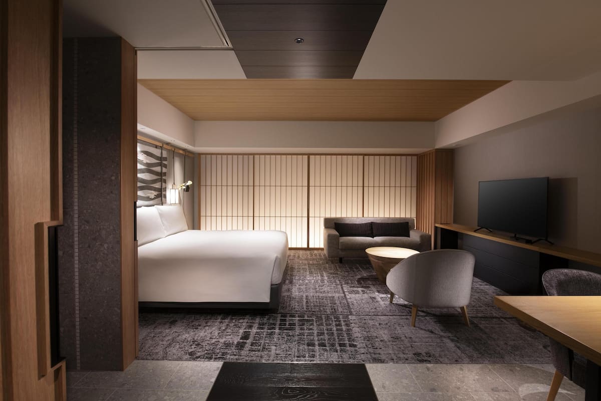 A modern hotel room with a large bed, a sofa, a TV, and a small table.