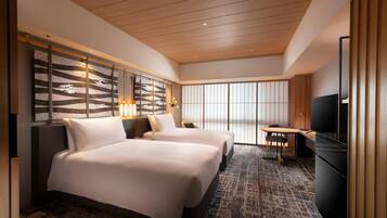 A hotel room with two beds, a TV, a small table, and a view of the outside through large windows.