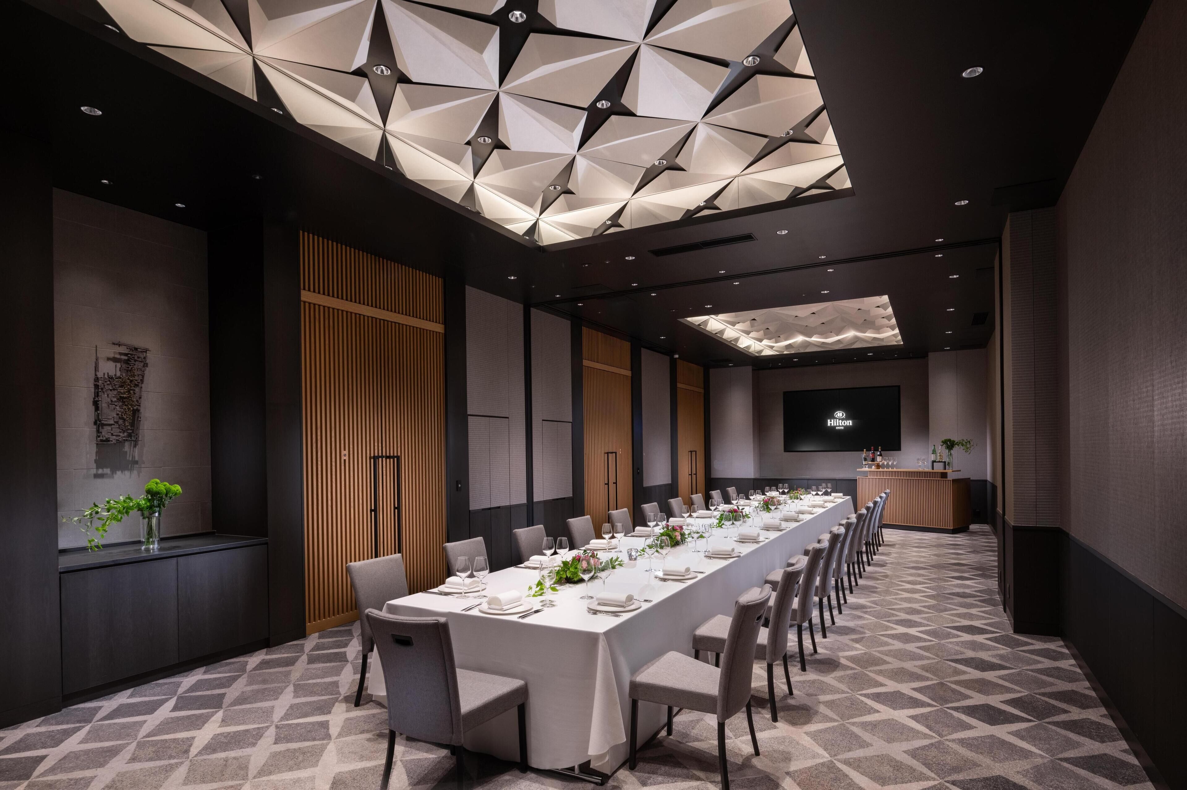 A conference room with a long table set for a meeting, a large screen, and a modern ceiling design.