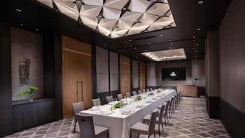 A conference room with a long table set for a meeting, a large screen, and a modern ceiling design.