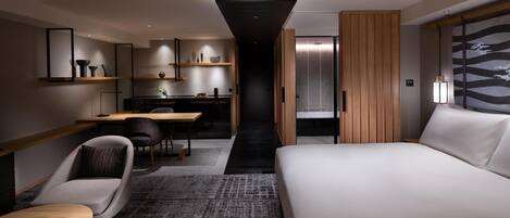 A modern hotel room with a large bed, a desk, a chair, and a small table. There is a wardrobe and a mirror on the wall.
