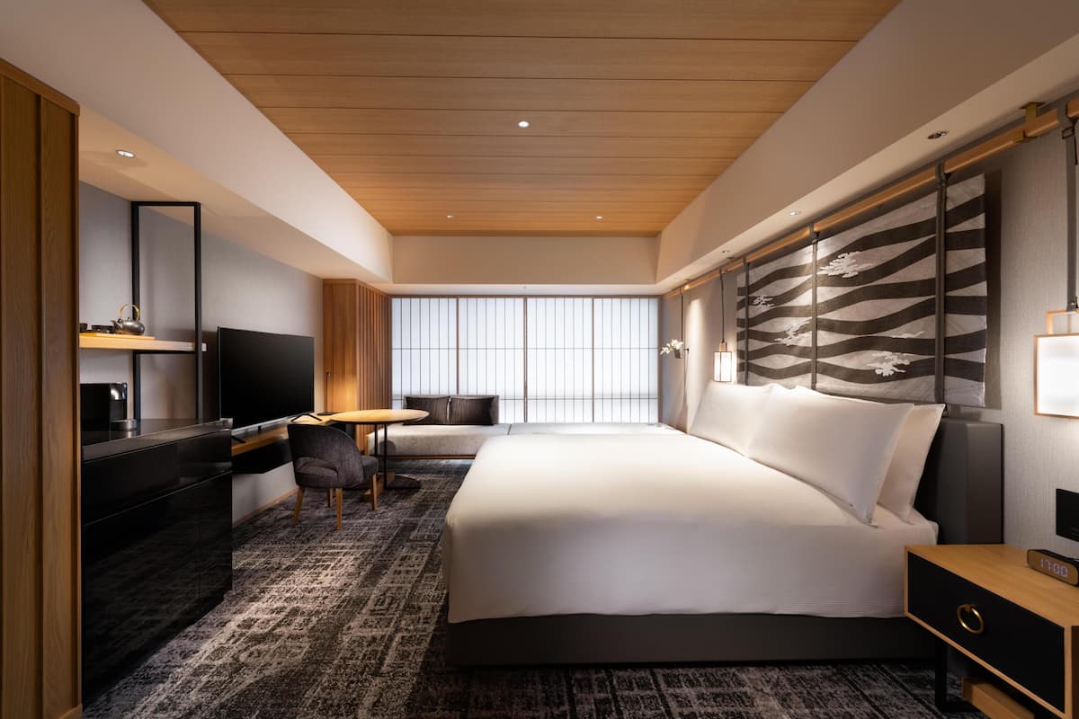A modern hotel room with a large bed, a desk with a chair, a TV, and a large window with a view.