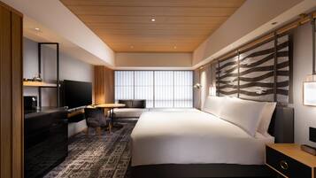 A modern hotel room with a large bed, a desk with a chair, a TV, and a large window with a view.