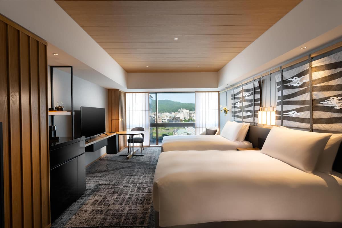 A modern hotel room with a large bed, a desk with a TV, and a view of the city.