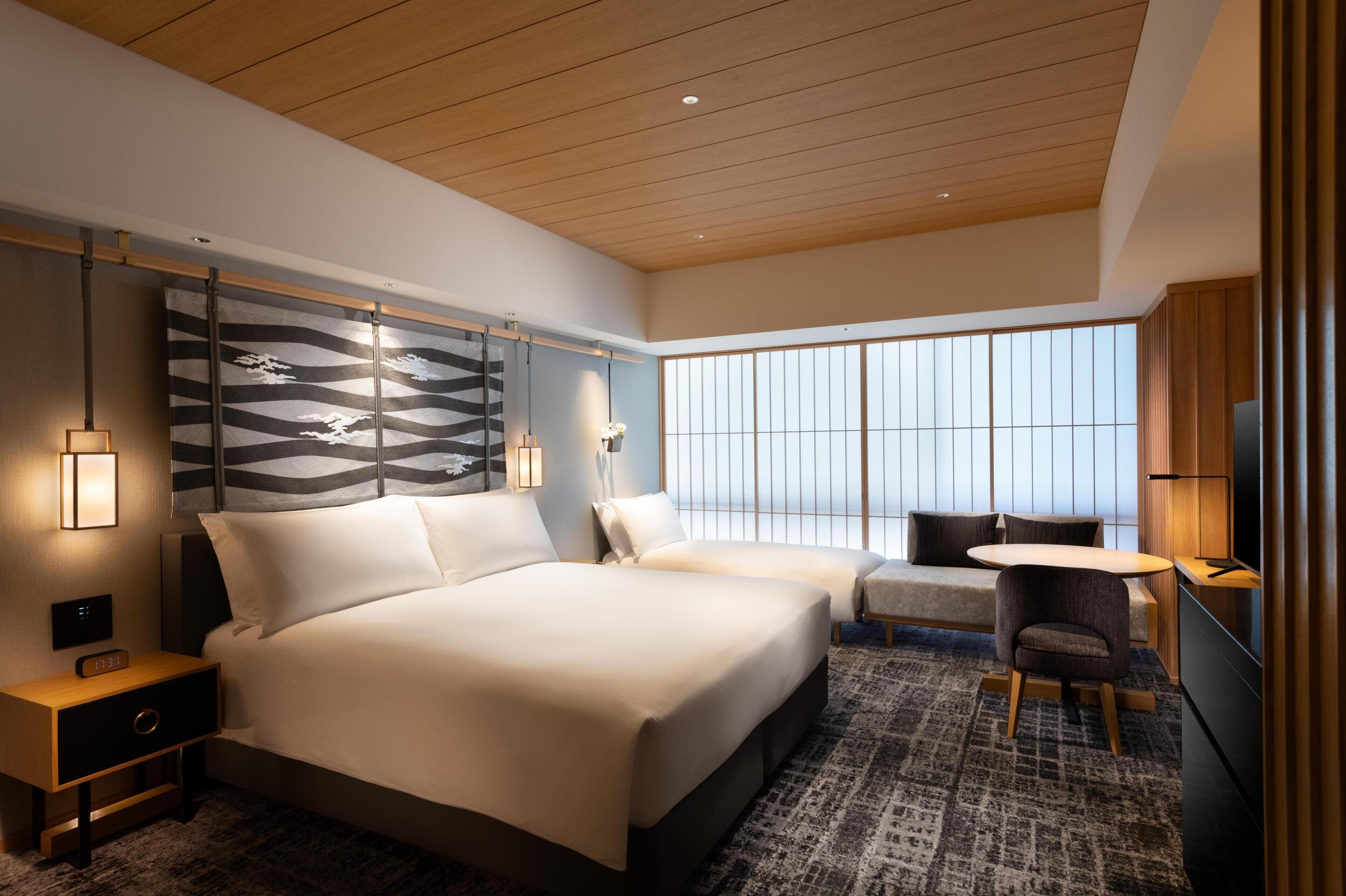 A modern hotel room with a large bed, a sofa, a small table, and a TV.