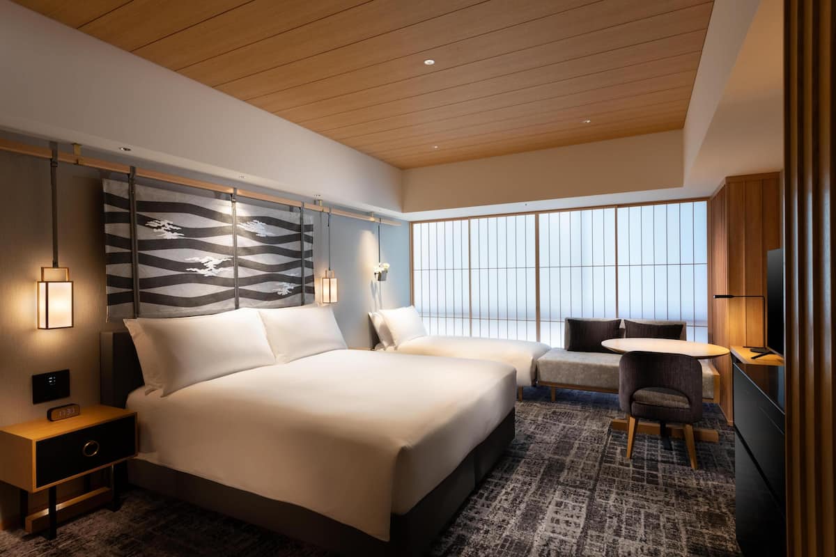A modern hotel room with a large bed, a sofa, a small table, and a TV.
