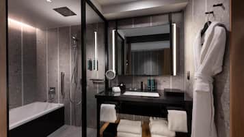 A modern bathroom with a glass-enclosed shower, a standalone bathtub, a black vanity with a mirror, and a white robe hanging on the wall.