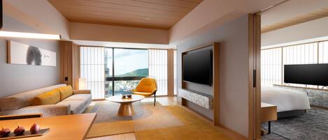 Quarto de hotel moderno com teto de madeira, uma televisão grande, um sofá, uma mesa de jantar e uma cama.
