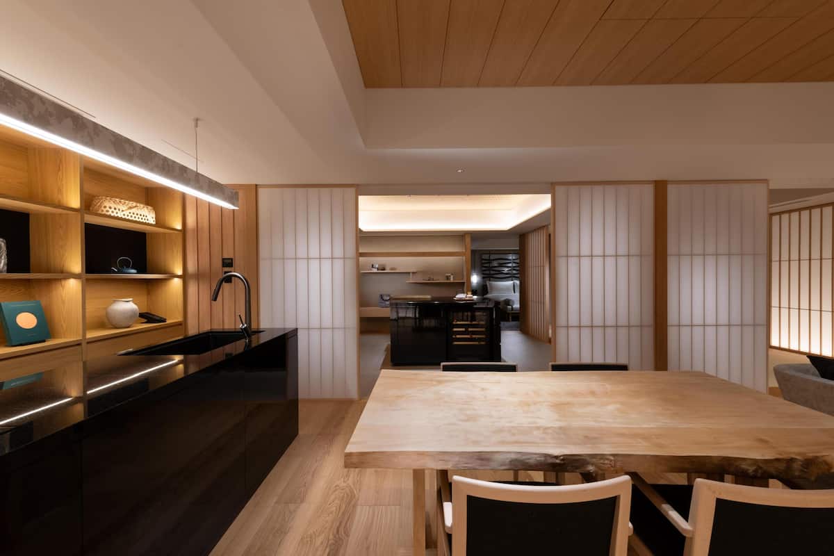 A modern kitchen with wooden cabinetry, a black countertop, and a wooden dining table.