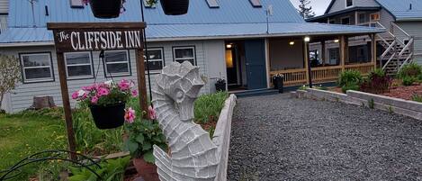 The Cliffside Inn with a stone sculpture, a blue metal roof, and a gravel driveway.