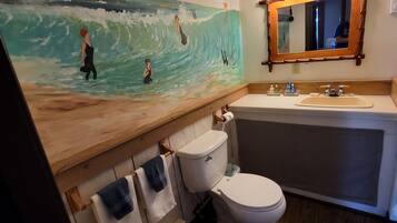 Et badeværelse med et stort billede af surfere, et trækommode, et badekar og et toilet.