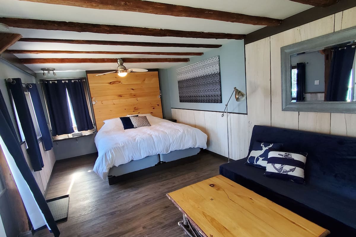 A compact room with a bed, a sofa, a wooden coffee table, and a ceiling fan.