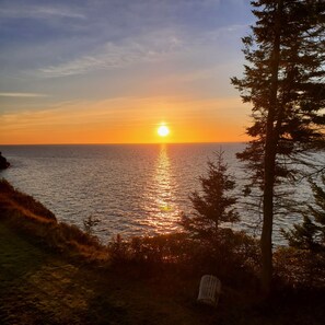 A sunset over a body of water with a chair and trees in the foreground.