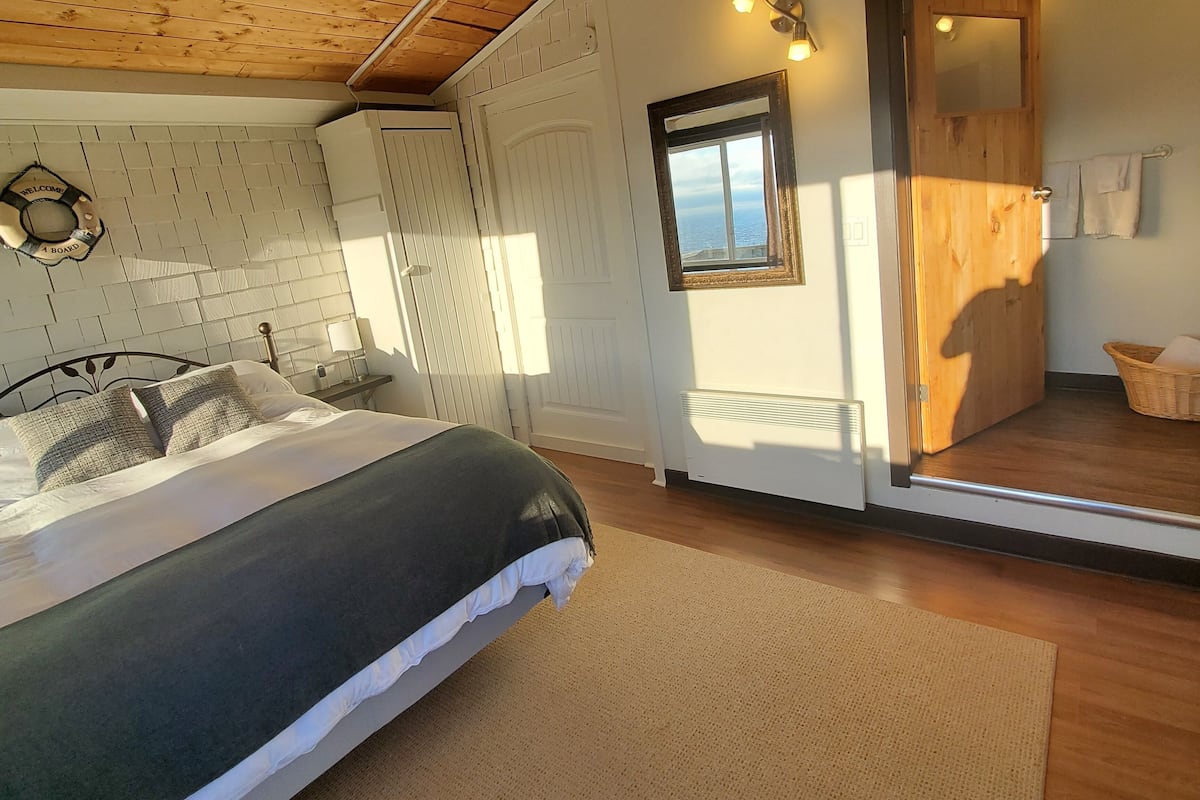 A bedroom with a bed, wooden ceiling, and a view through an open door.