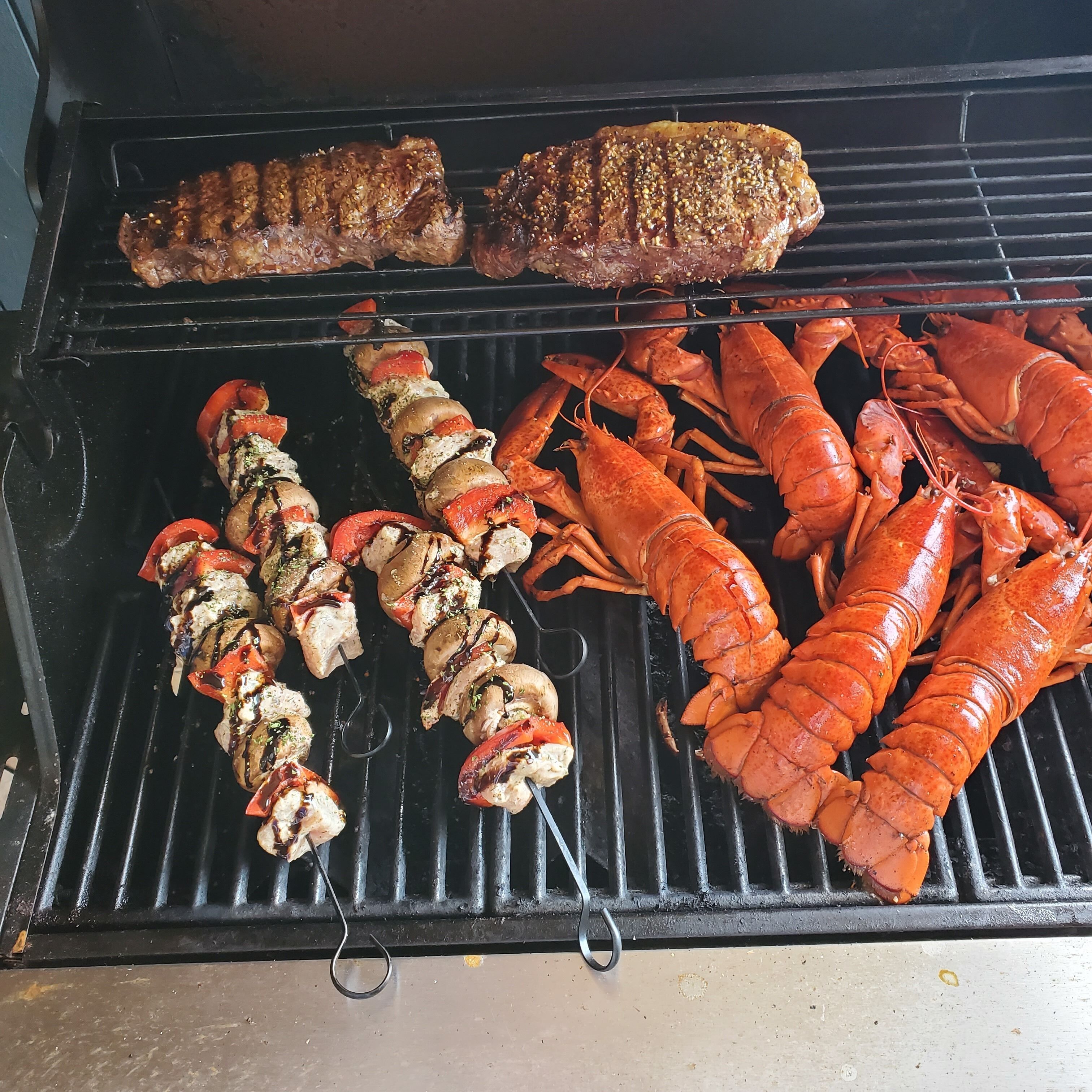 A grill with various meats and seafood being cooked.