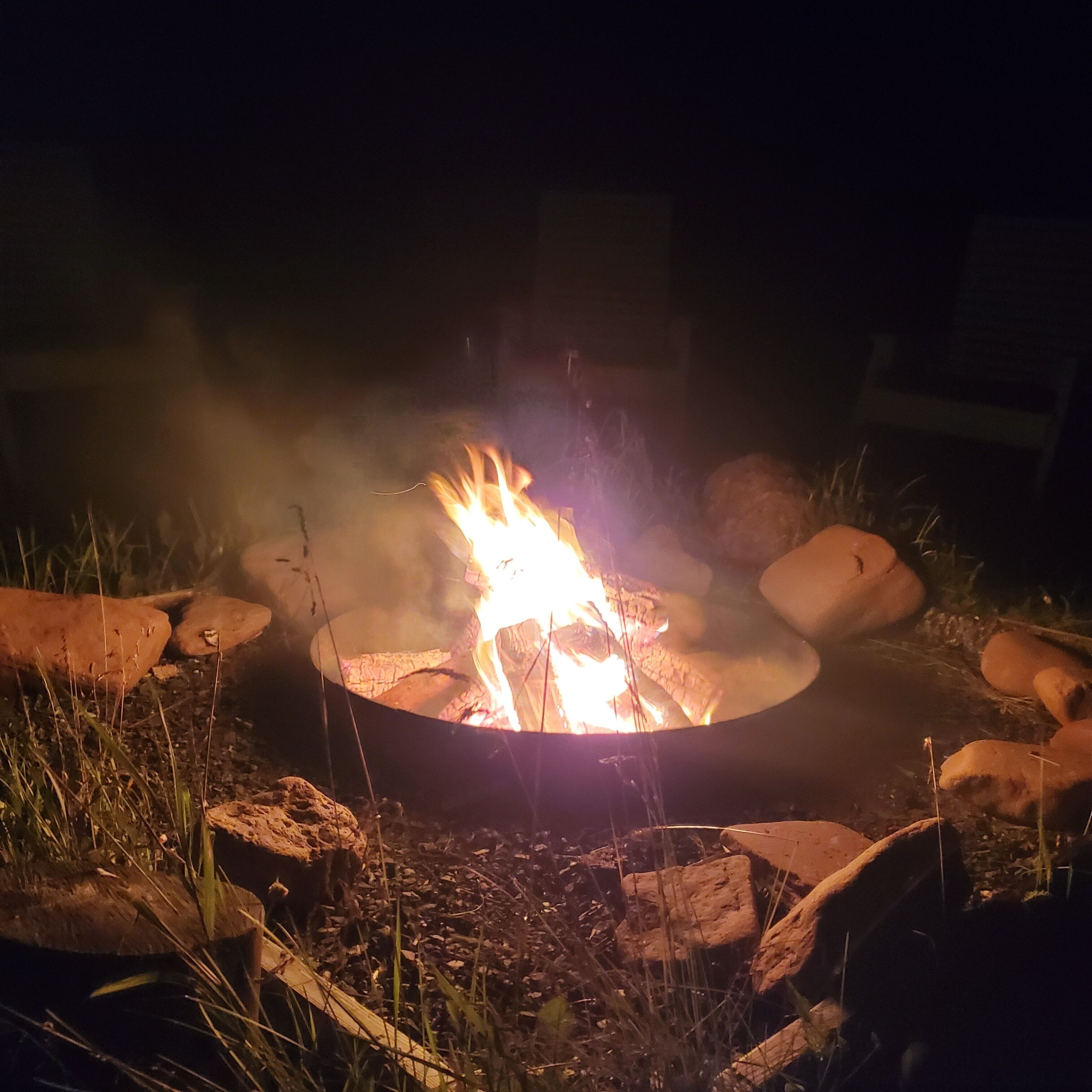 A campfire with logs arranged in a circle, surrounded by rocks and grass.