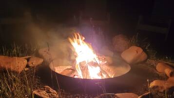 A campfire with logs arranged in a circle, surrounded by rocks and grass.