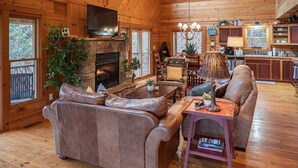 Ein gemütliches Blockhaus-Interieur mit Kamin aus Stein, Ledersofas, einem Essbereich und einer Küche mit Holzausbau.