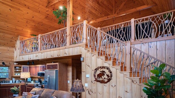 Ein Holzhütten-Interieur mit Küche, Wohnbereich und einer Treppe mit ungewöhnlichem Geländerdesign.
