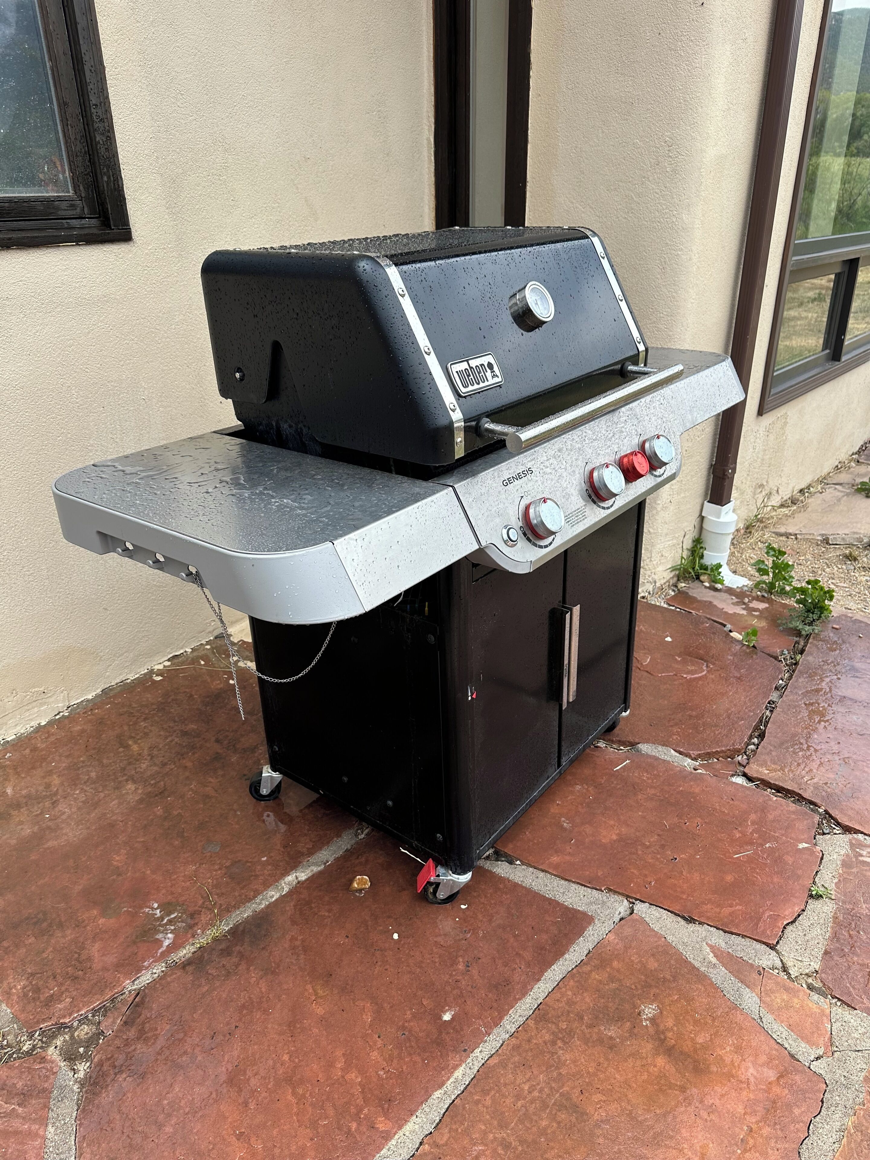 Una parrilla Genesis portátil con una mesita auxiliar, ubicada en un patio de piedra.