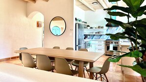Un comedor con una mesa y sillas de madera, un ventilador de techo y una cocina al fondo.