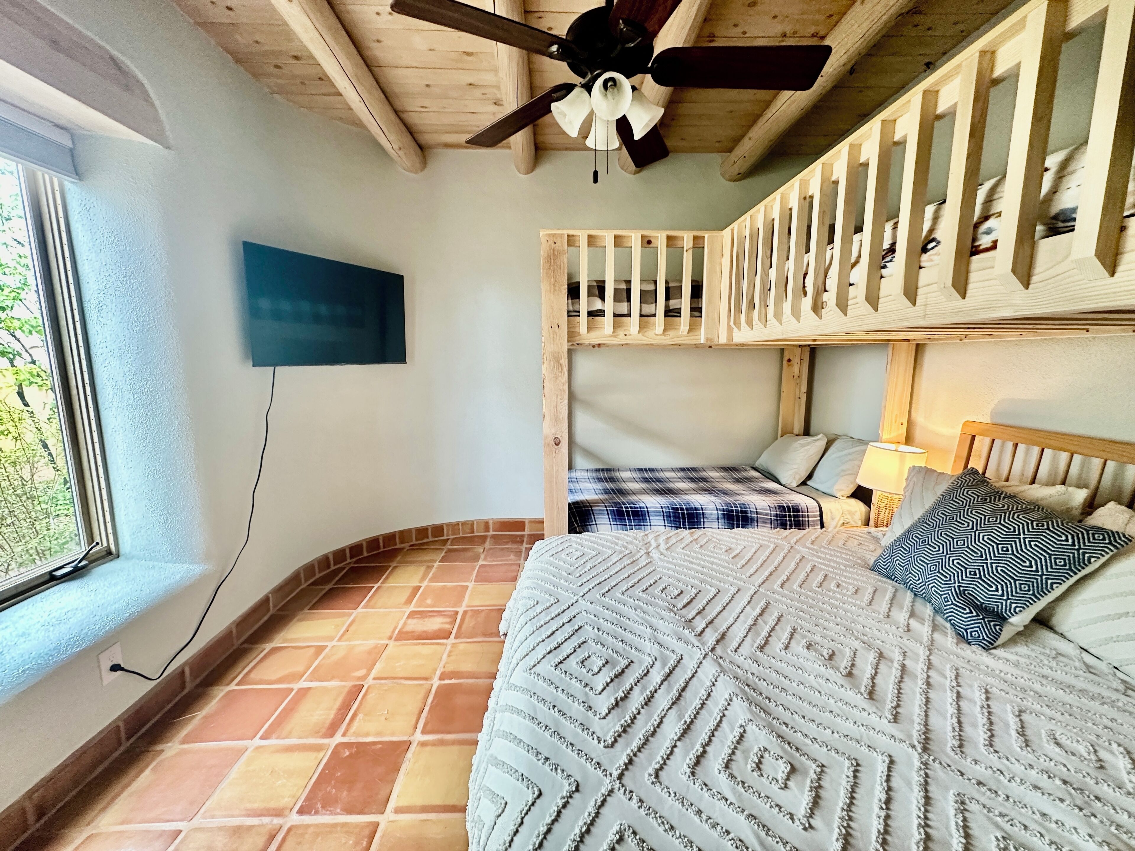 Une pièce avec un plafond en bois, un lit avec une literie à motifs, une fenêtre donnant sur un beau paysage et un téléviseur fixé au mur.