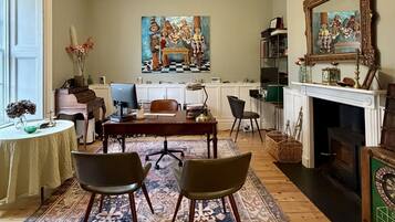 A room with a dining table, two chairs, a piano, a fireplace, and a painting on the wall.